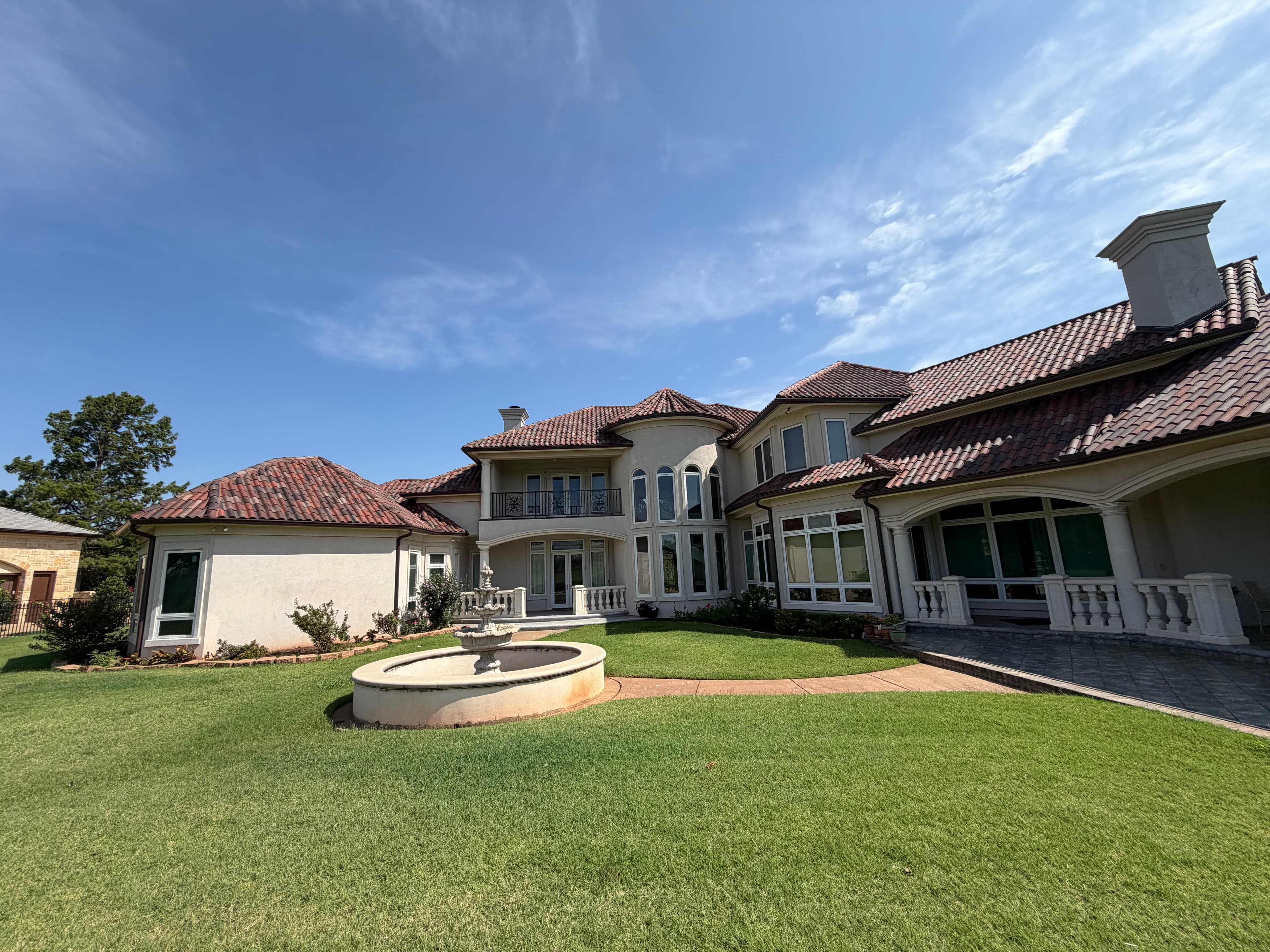 Luxurious Mediterranean mansion with red tile roof and stone fountain on a wide green lawn.
