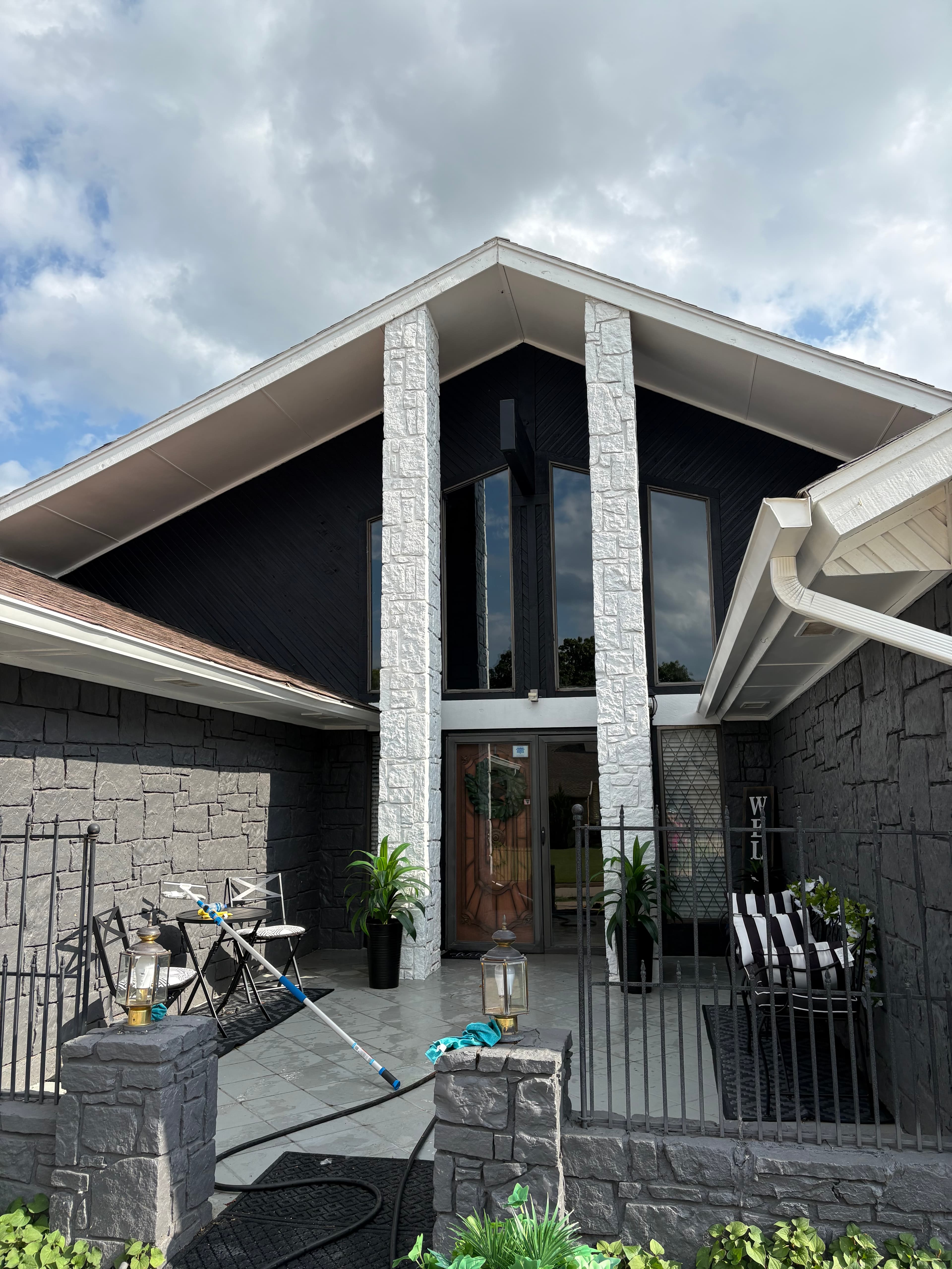Modern dark grey A-frame house featuring white stone pillars and a gated stone patio.