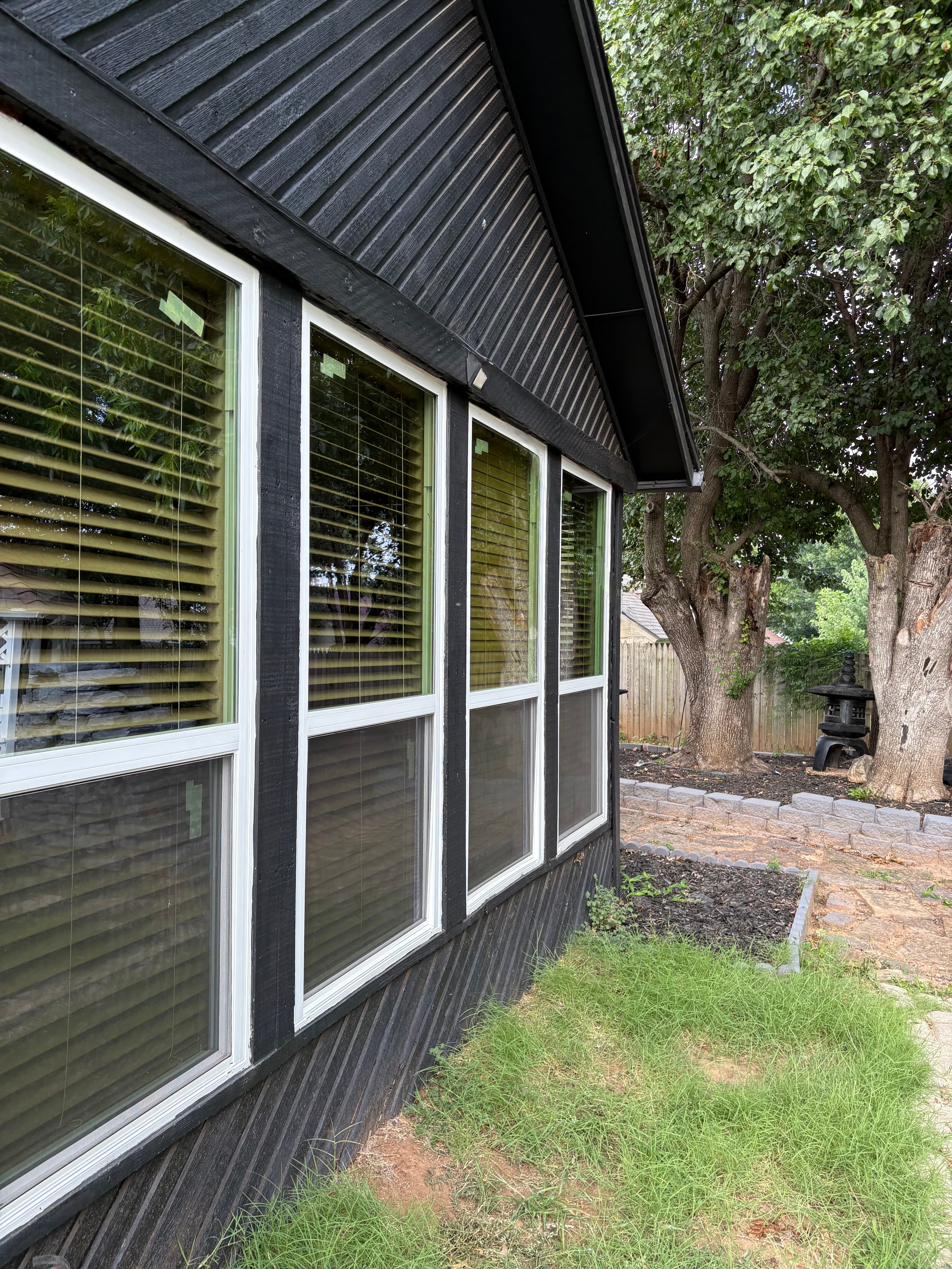 Black house with diagonal siding and four white windows overlooking a backyard with trees.