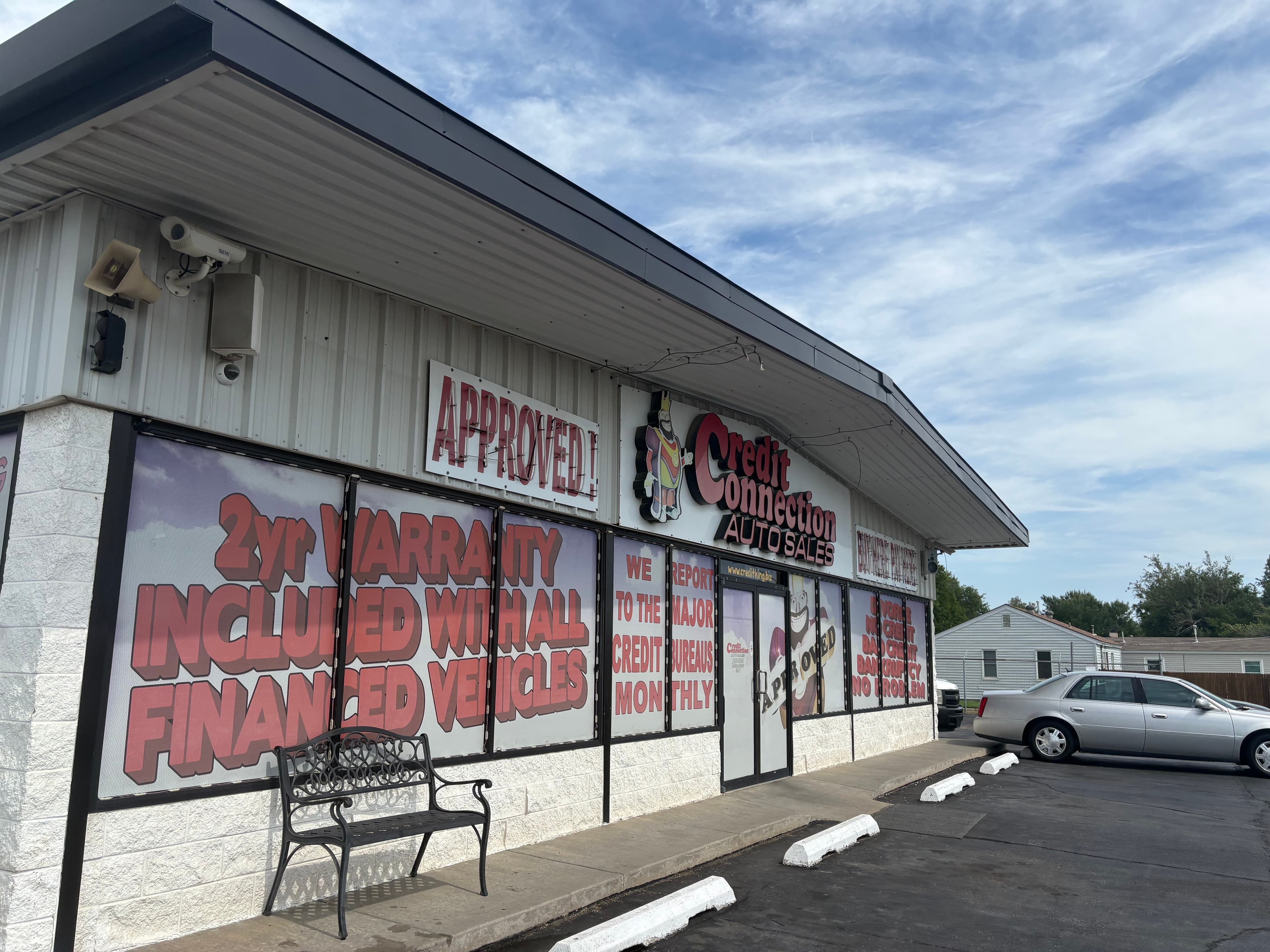 Credit Connection Auto Sales storefront with red window advertisements, a black bench, and silver car.