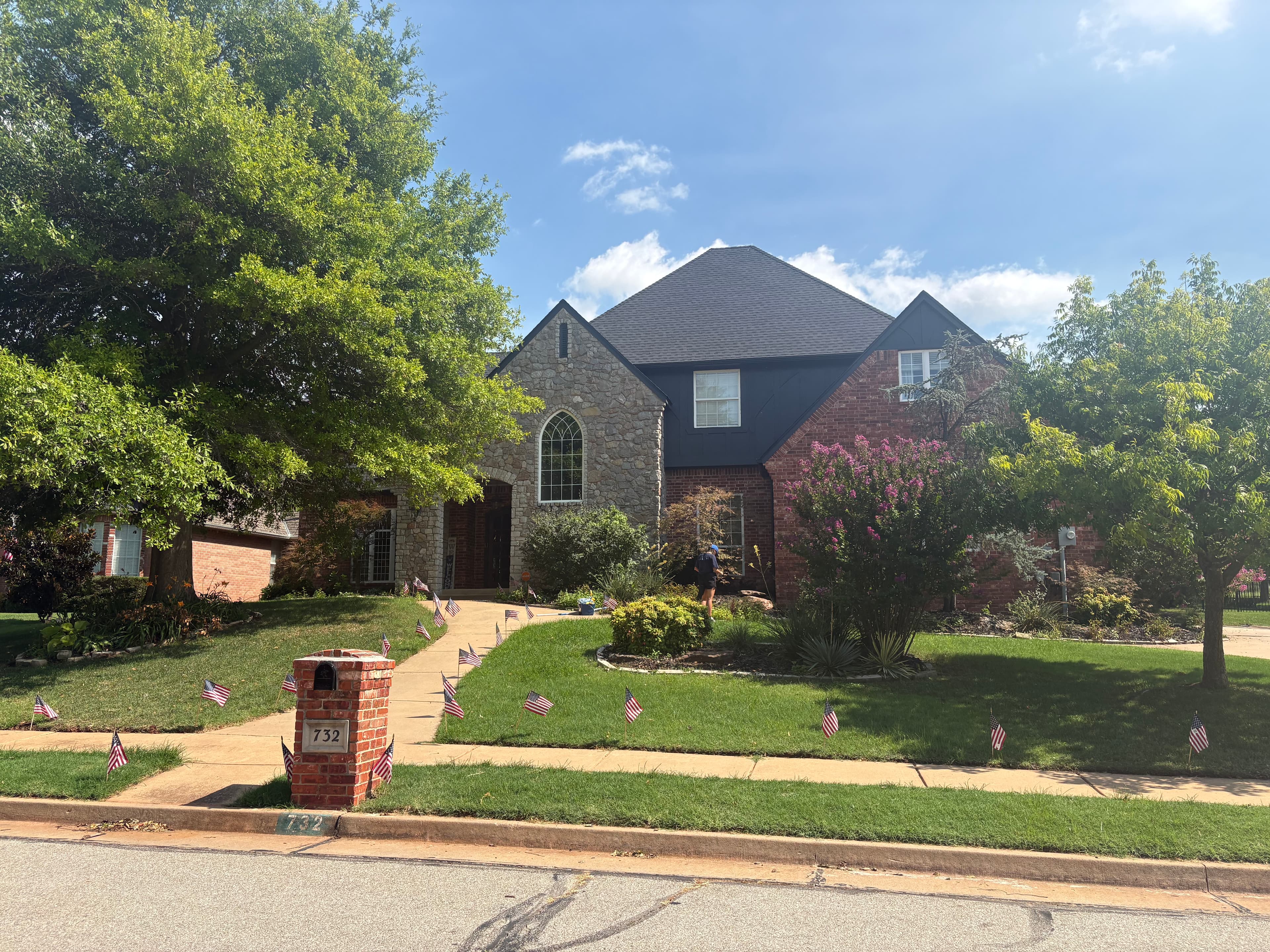 Large stone and brick house with small American flags lining the walkway and lawn.