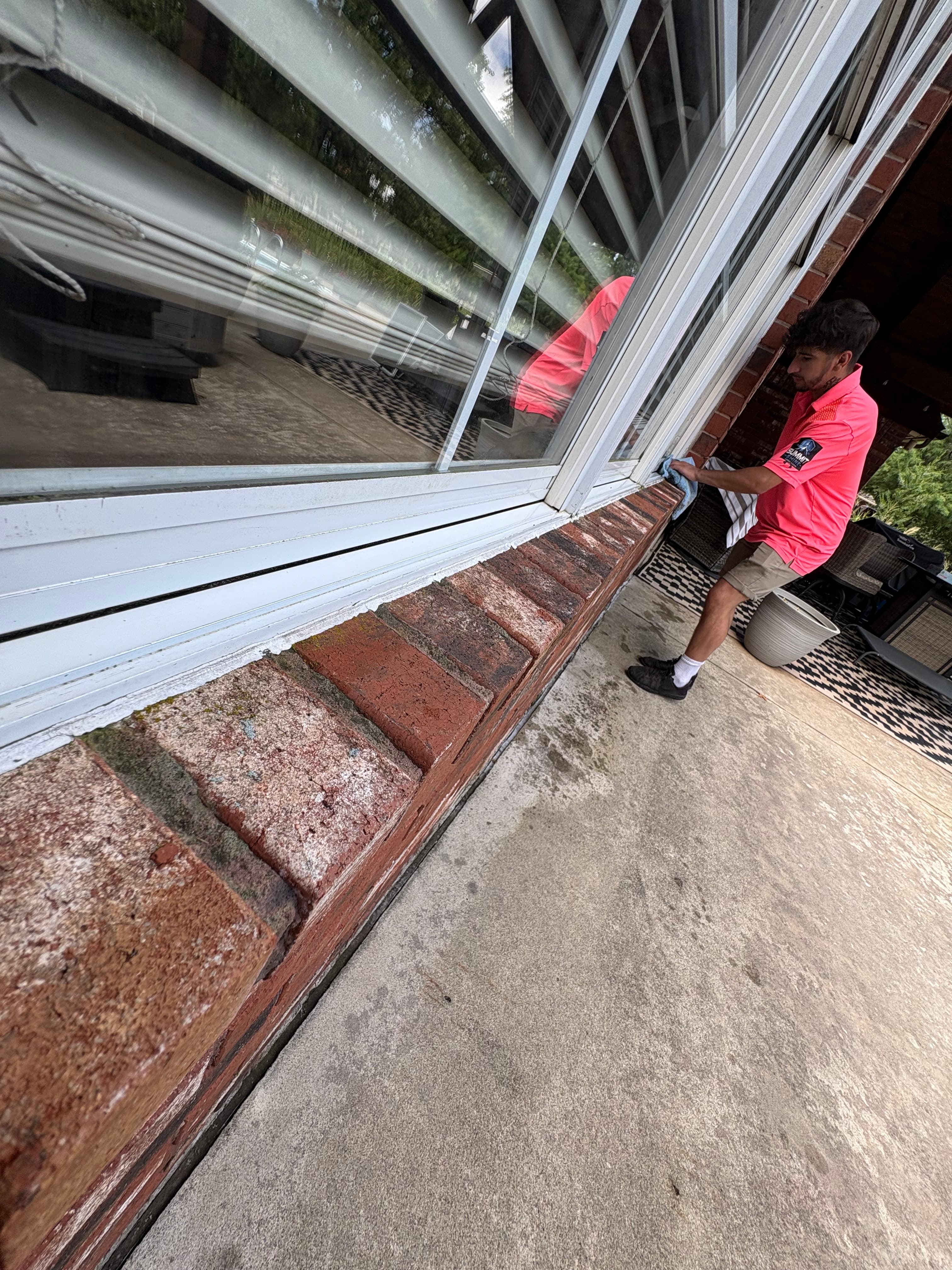 Man in a pink polo cleans a large exterior window with a blue cloth.