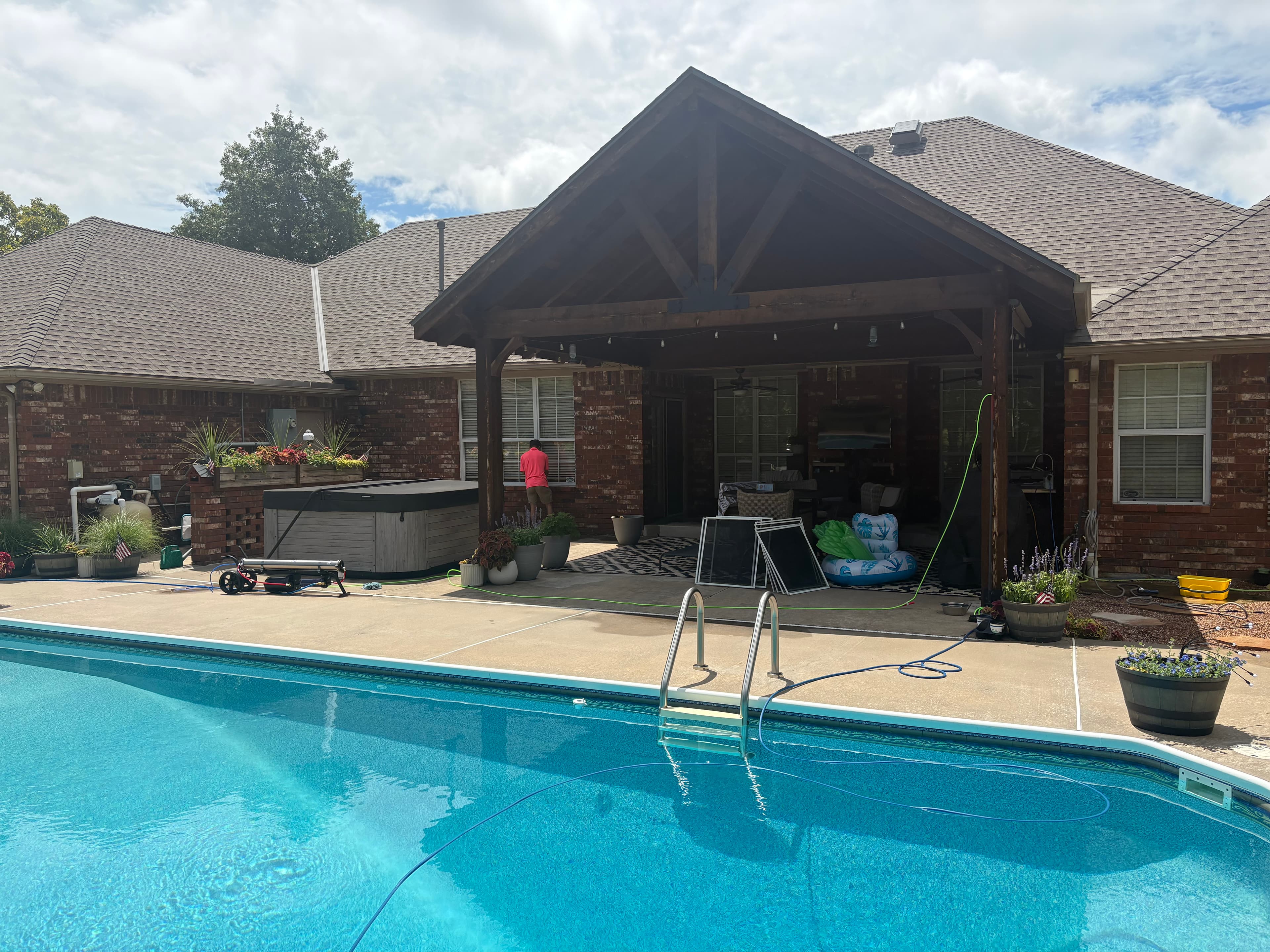 Backyard swimming pool and concrete deck with a large covered wooden patio and brick house.